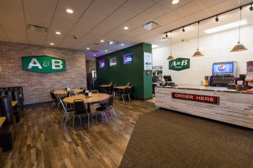 Interior of A&B Pizza restaurant featuring seating, a counter, and a menu display. Warm lighting and modern decor.